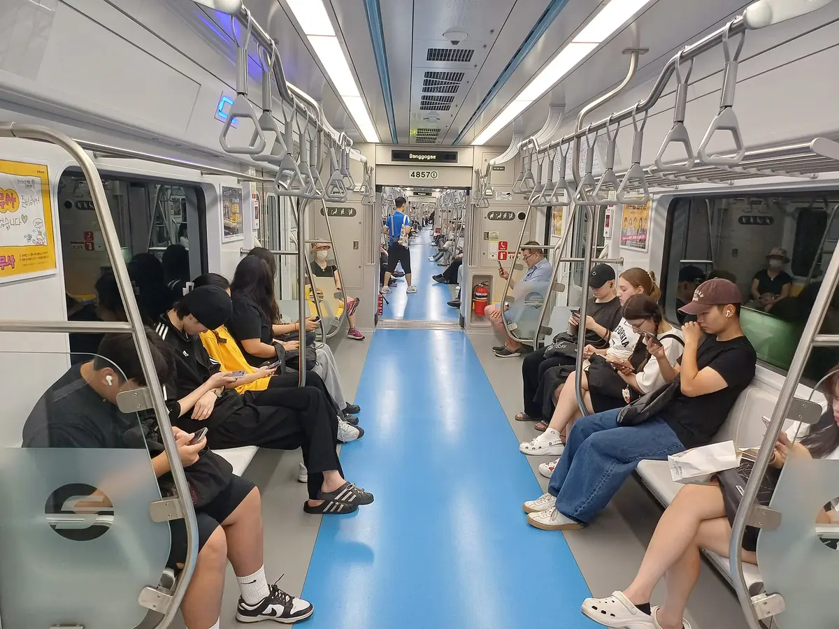 ソウル地下鉄4号線の車内。青い床と両側の座席、立っている乗客