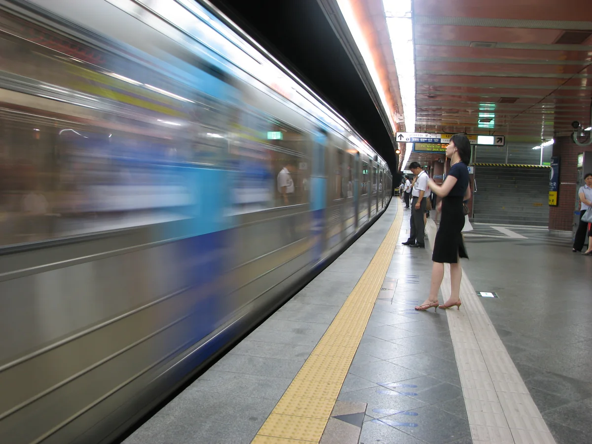 A Seoul subway train arriving at a platform, motion-blurred, with a waiting passenger