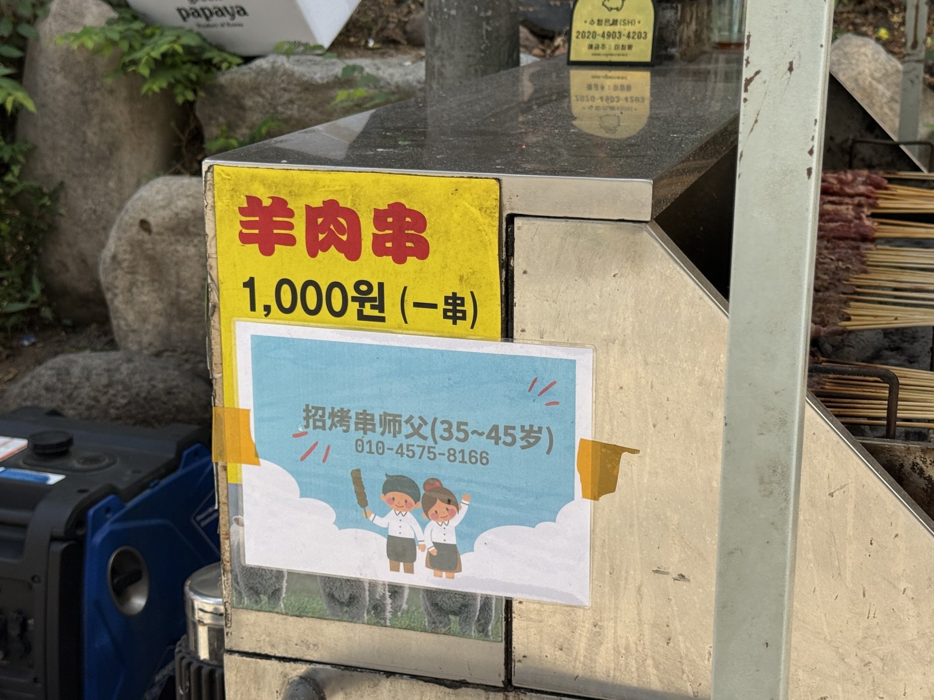 A price board reading 1,000 won per lamb skewer