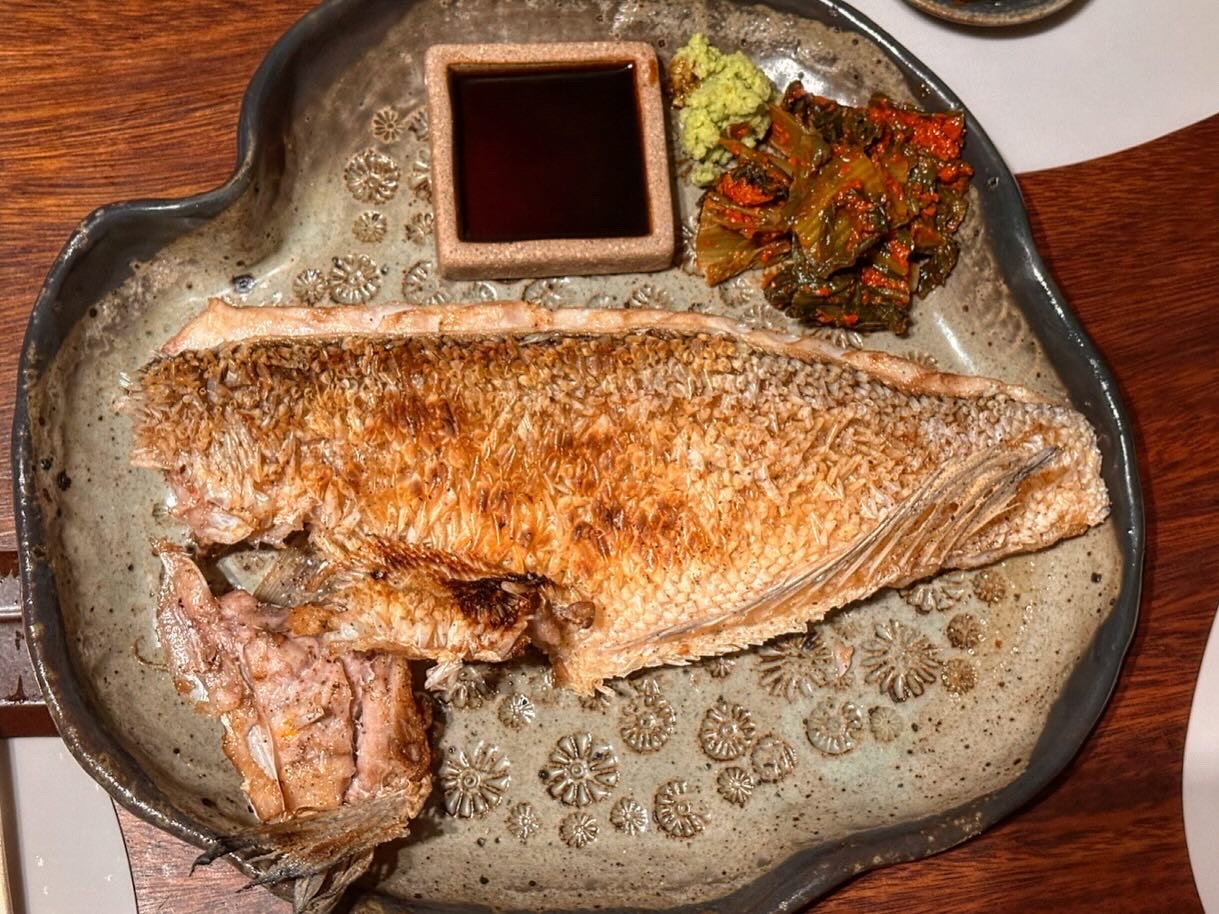 A whole grilled okdom with a dish of soy sauce and pickles