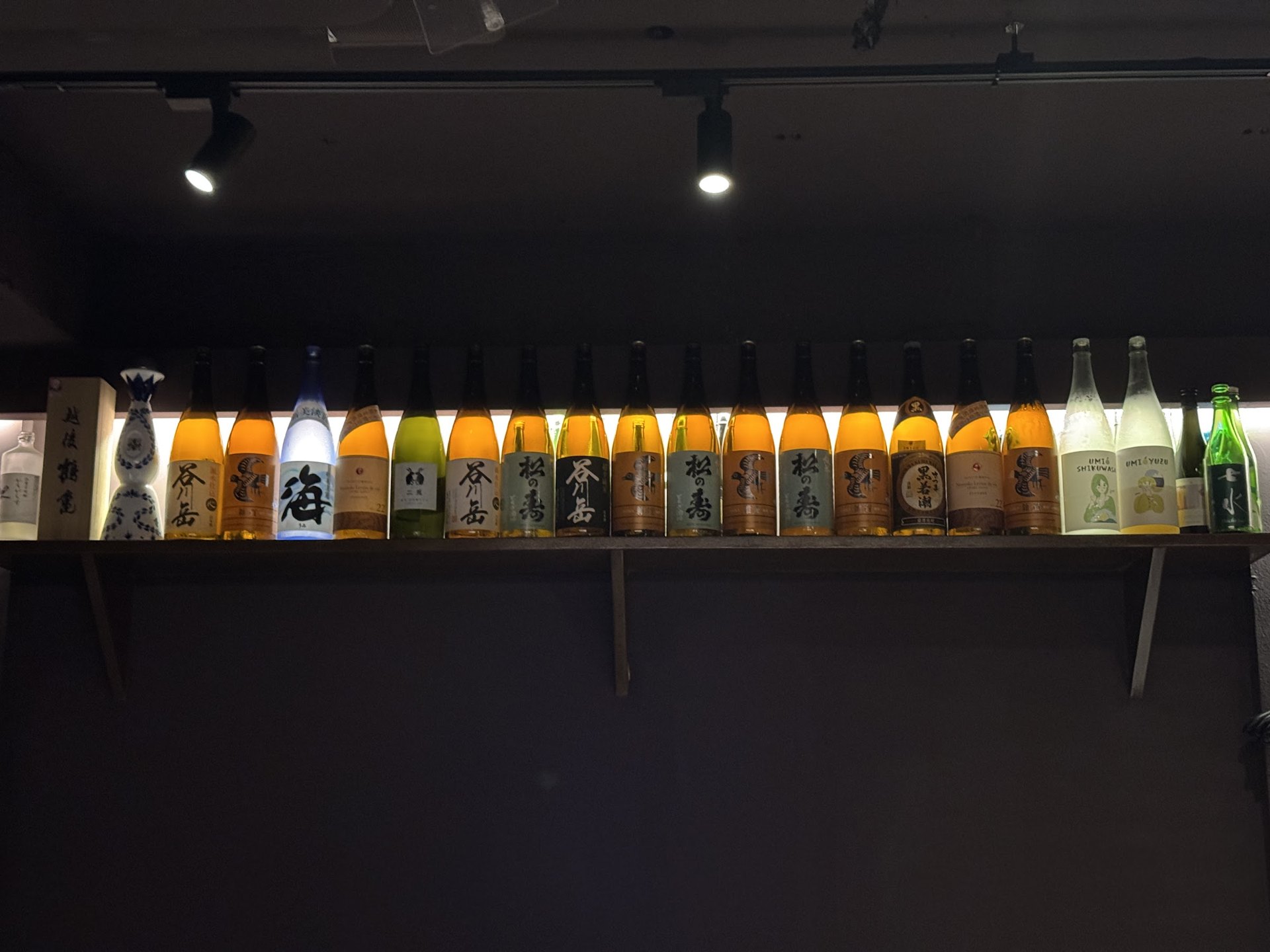 벽면 선반에 조명을 받고 늘어선 일본주 병들