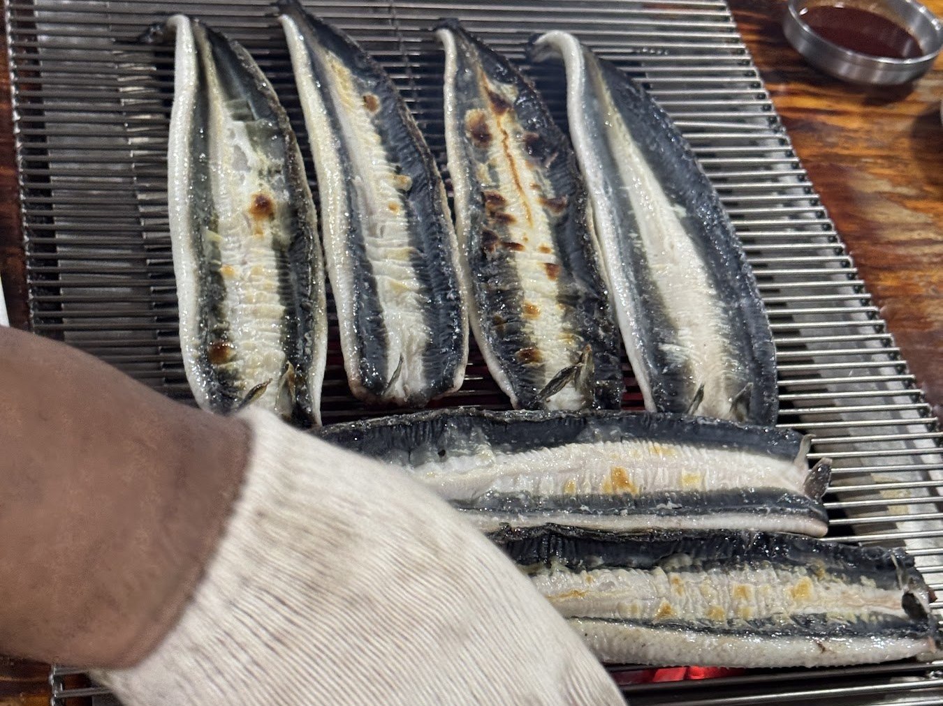 戴著手套的手在烤網上翻動鰻魚