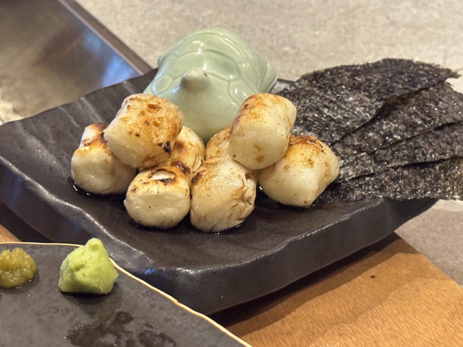 表面烤出焦痕的圓形料理，配上海苔與黃綠色醬汁