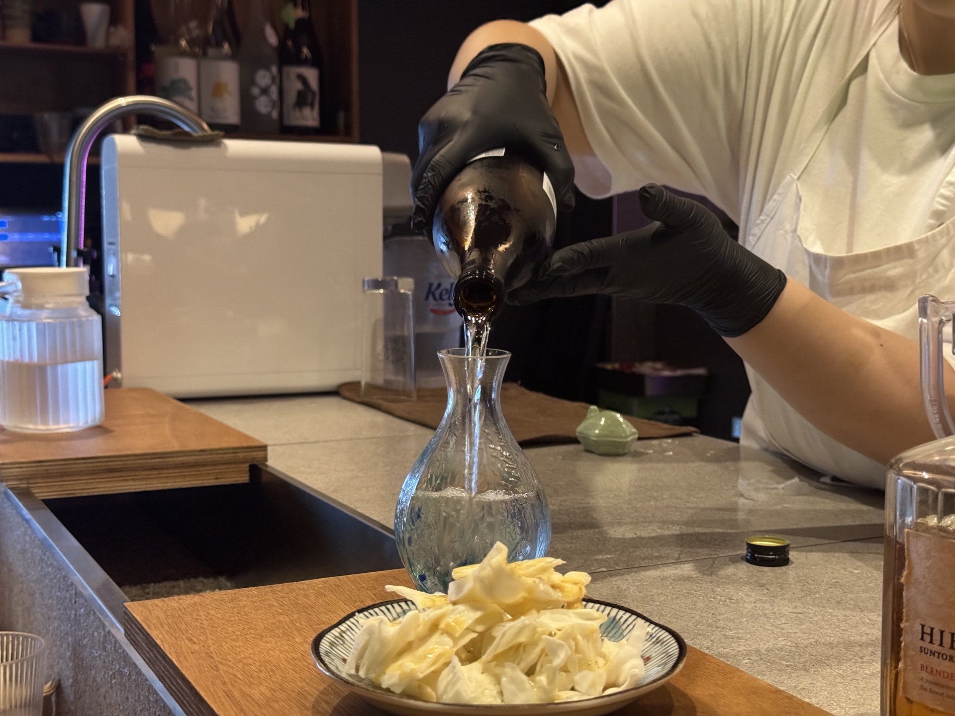 戴黑色手套的手將清酒倒入玻璃酒瓶