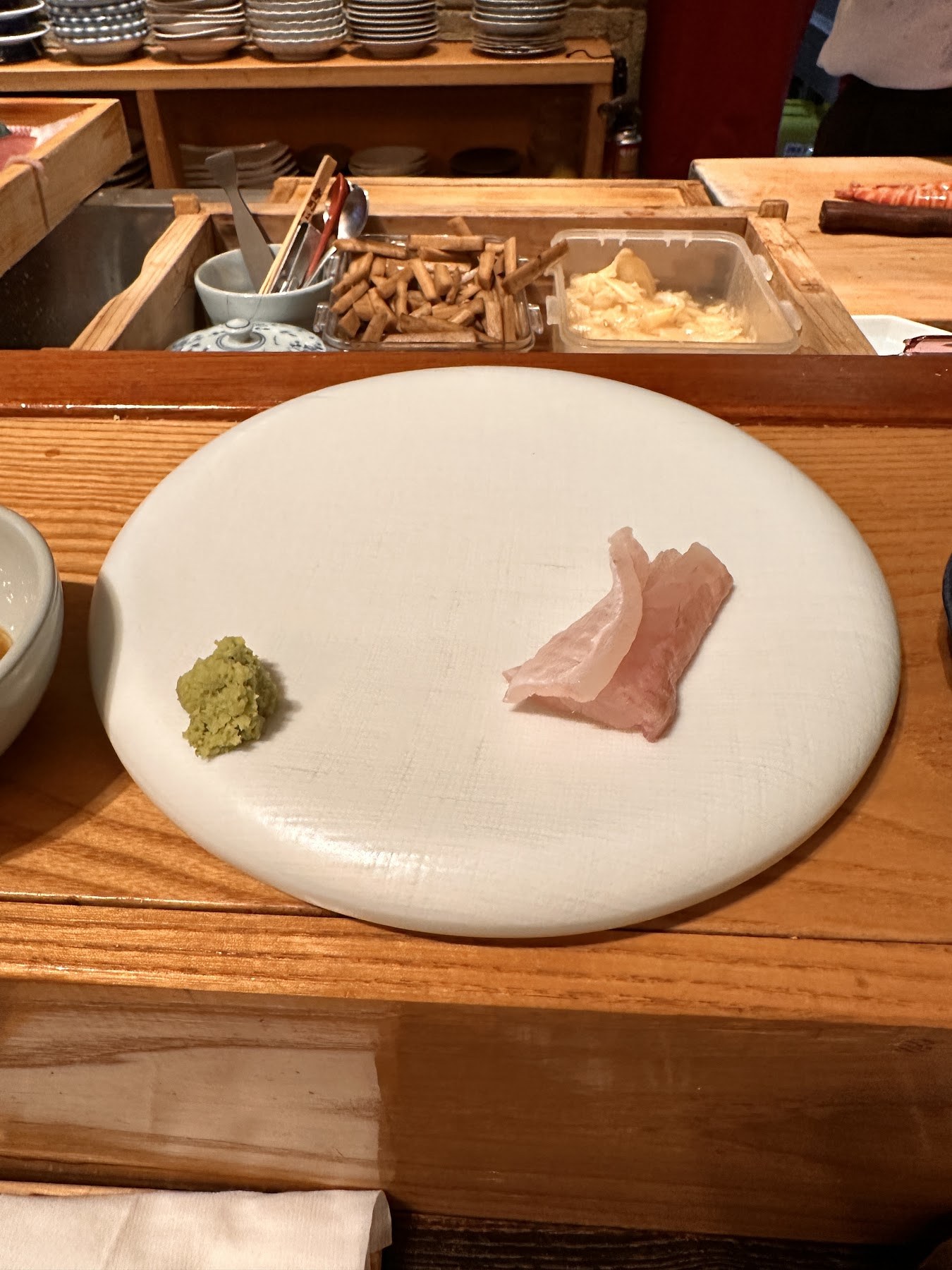 The first plate, a white dish with wasabi and a single piece of fish